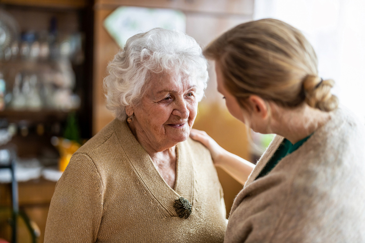 Adult daughter speaking gently with her elderly mother at home, offering reassurance and support