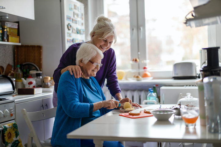 Older woman preparing food in her kitchen with supportive help from a companion